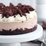A whole Brownie Batter Cheesecake with layers of brownie crust, creamy cheesecake filling, whipped cream, crumbled brownies, and hot fudge sauce.