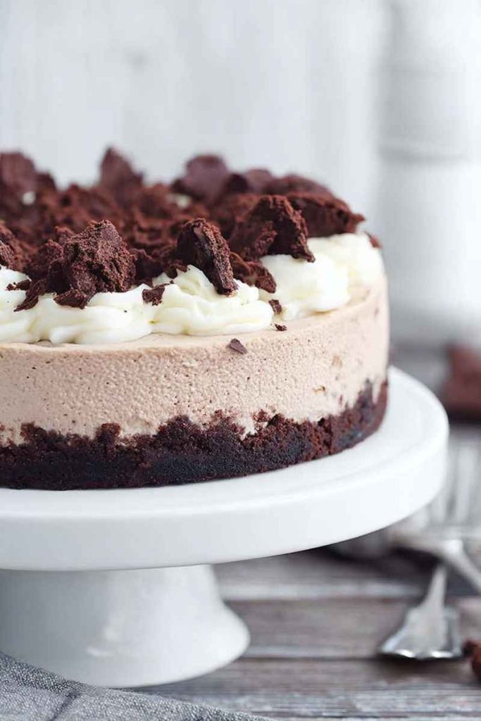 A whole Brownie Batter Cheesecake with layers of brownie crust, creamy cheesecake filling, whipped cream, crumbled brownies, and hot fudge sauce.
