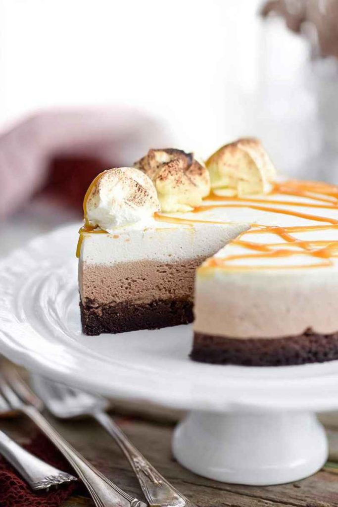 A partially sliced Caramel Hot Chocolate Brownie Mousse Cake with layers of brownie crust, hot chocolate mousse, caramel whipped cream, and caramel drizzle.