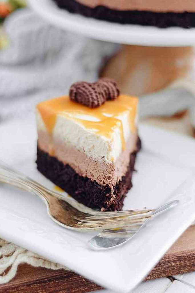 A slice of Caramel Hot Chocolate Brownie Mousse Cake with layers of brownie crust, hot chocolate mousse, caramel whipped cream, and caramel drizzle.