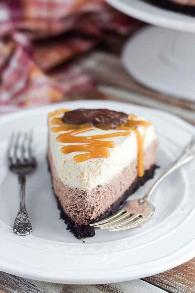 A slice of Caramel Hot Chocolate Brownie Mousse Cake with layers of brownie crust, hot chocolate mousse, caramel whipped cream, and caramel drizzle.