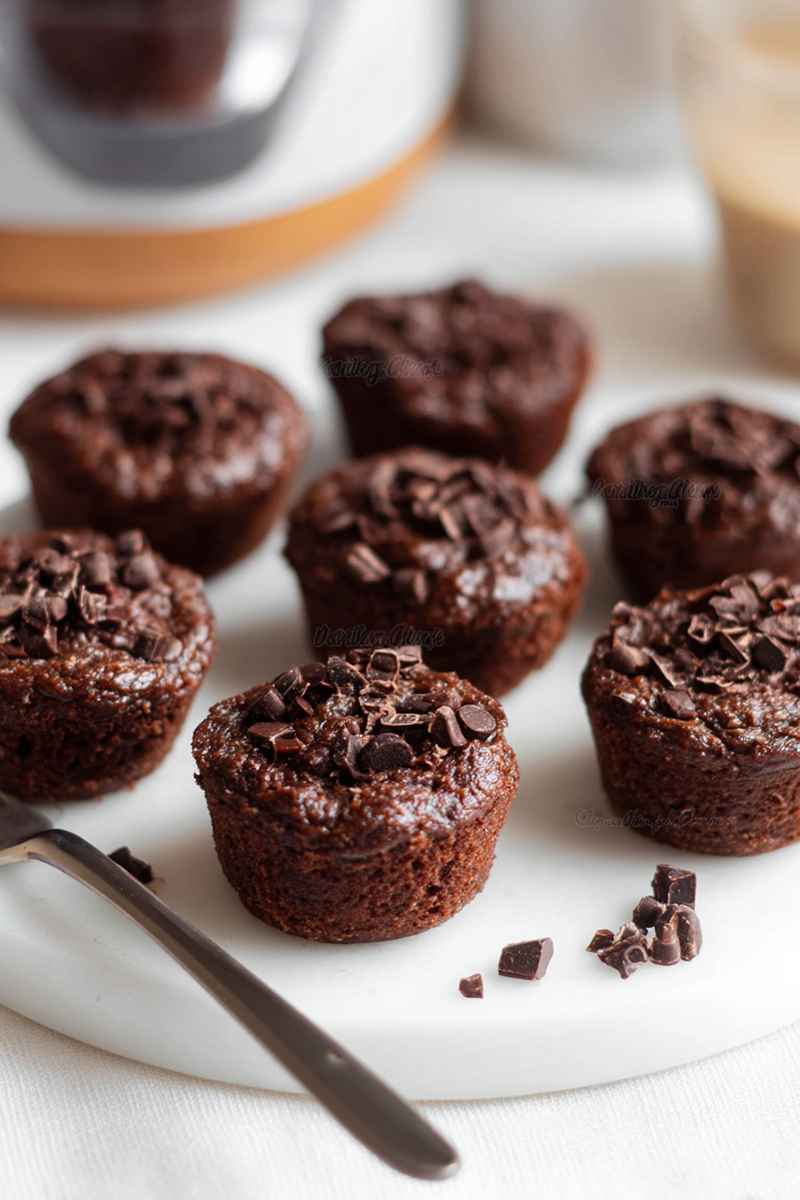 Chocolate muffins topped with chocolate shavings and chips, served on a white plate with scattered chips around.