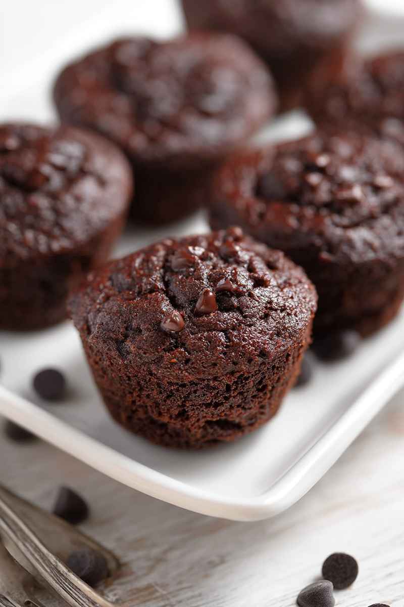 Close-up of a moist chocolate muffin with visible chocolate chips, served on a white plate.