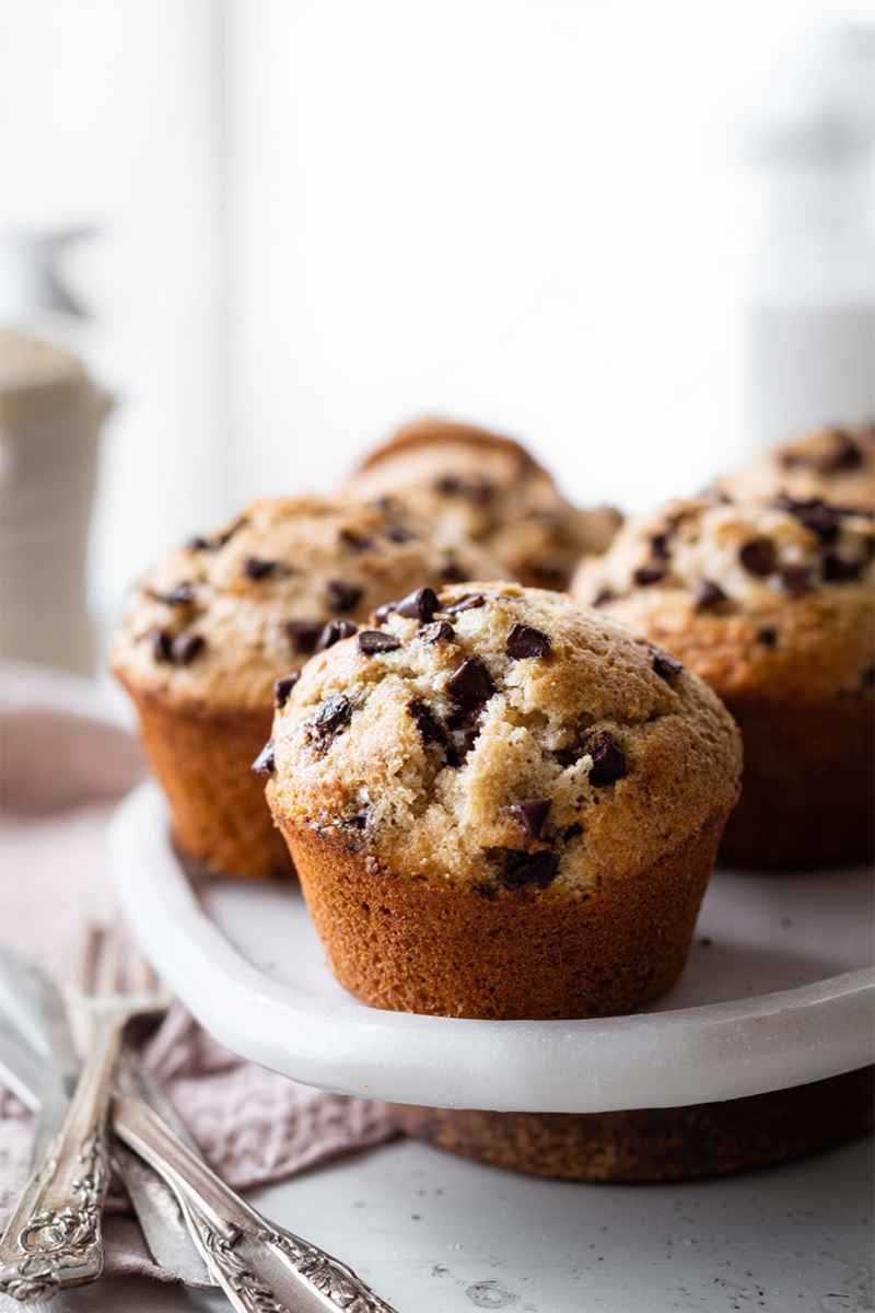 Close-up of Chocolate Chip Muffins on a white plate, emphasizing their golden texture and sprinkled chocolate chips.