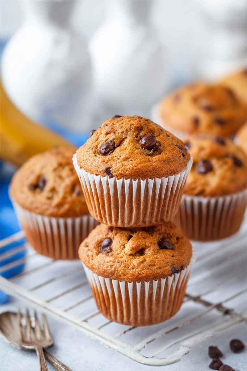 Golden-brown banana chocolate chip muffins on a cooling rack, with scattered chocolate chips and vintage forks nearby.
