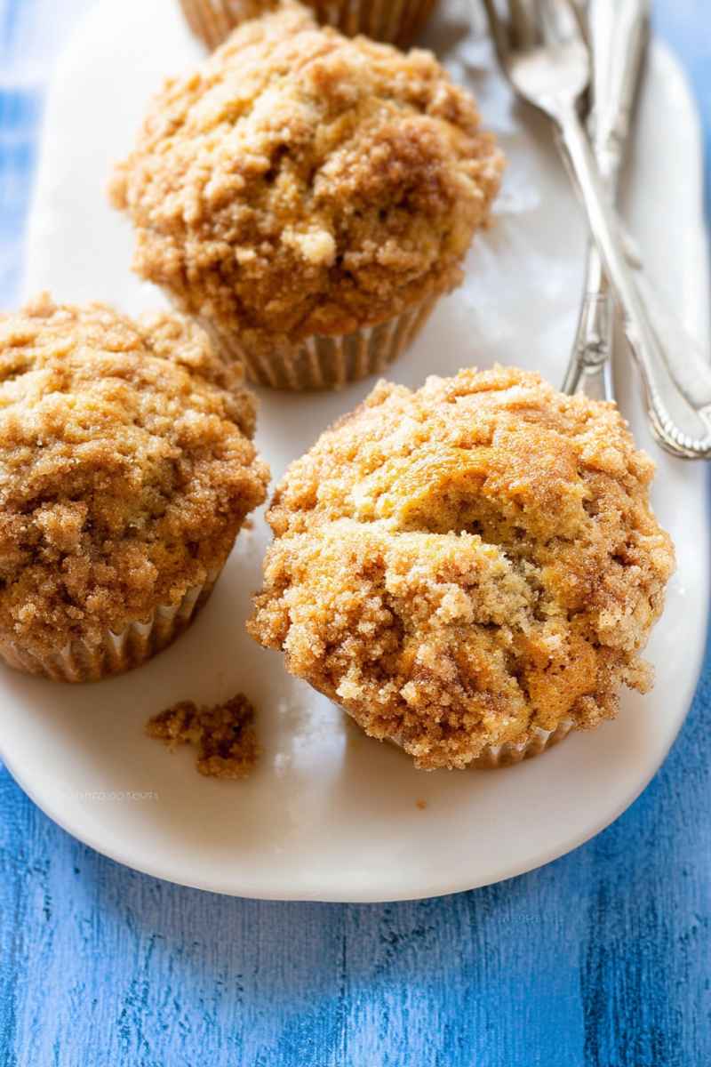 Golden banana muffins with a cinnamon-sugar crumble topping, served on a white plate.