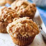 Golden banana muffins topped with a cinnamon-sugar crumble, served on a white plate.