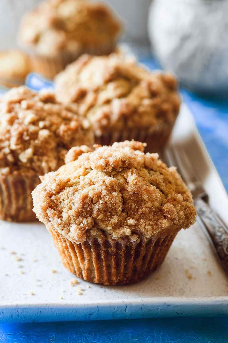 Golden banana muffins topped with a cinnamon-sugar crumble, served on a white plate.