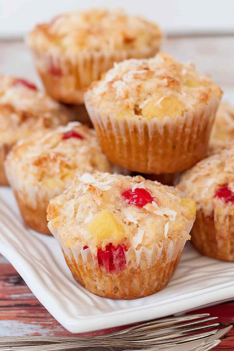 A close-up of banana pineapple muffins with coconut shreds and maraschino cherries, showcasing their moist and fluffy texture.