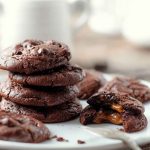 A stack of Chocolate Caramel Cookies with one cookie broken in half, revealing the gooey caramel filling.