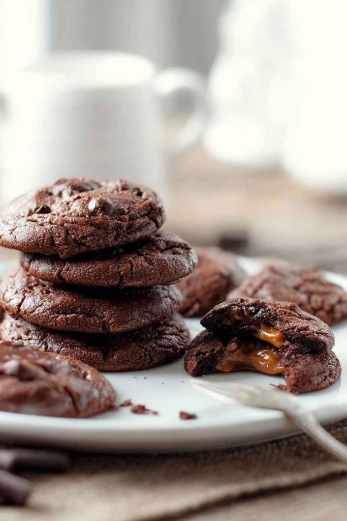 A stack of Chocolate Caramel Cookies with one cookie broken in half, revealing the gooey caramel filling.