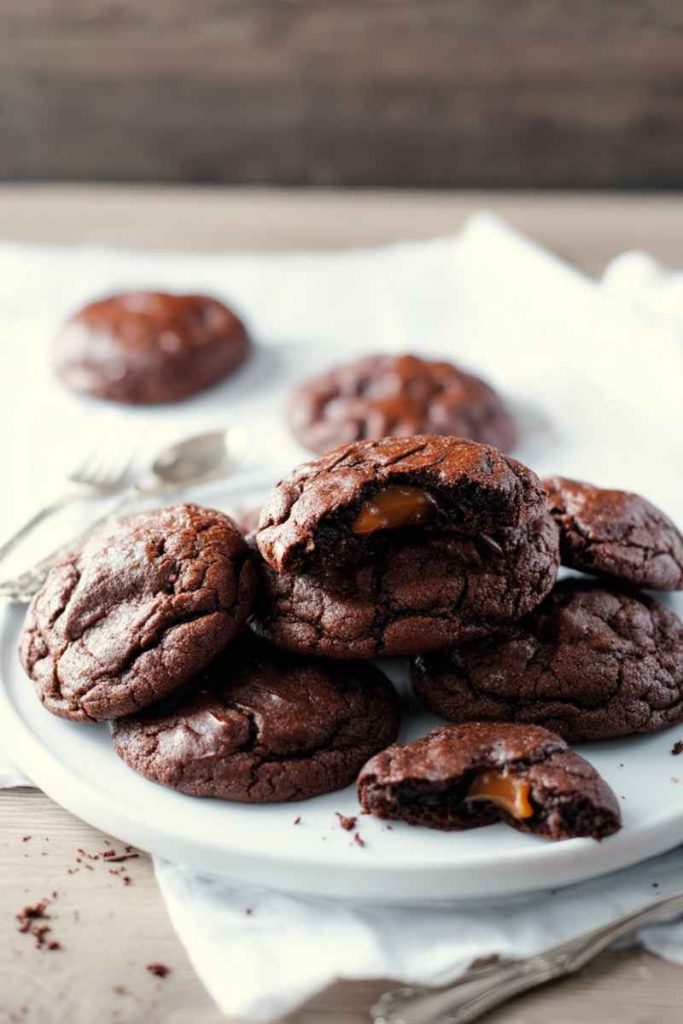 A plate of Chocolate Caramel Cookies with one cookie broken in half, revealing the gooey caramel filling.