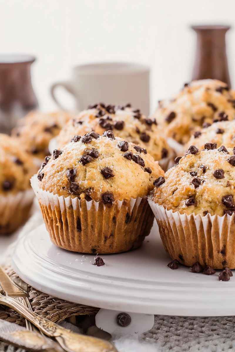Golden chocolate chip muffins with mini chocolate chips, served on a white plate.