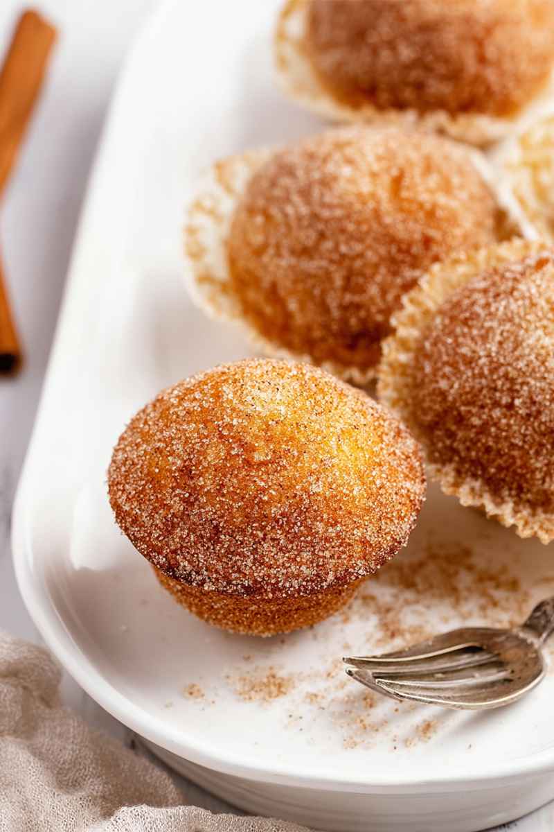 Close-up of a mini muffin coated in cinnamon sugar, with a cinnamon stick in the background.
