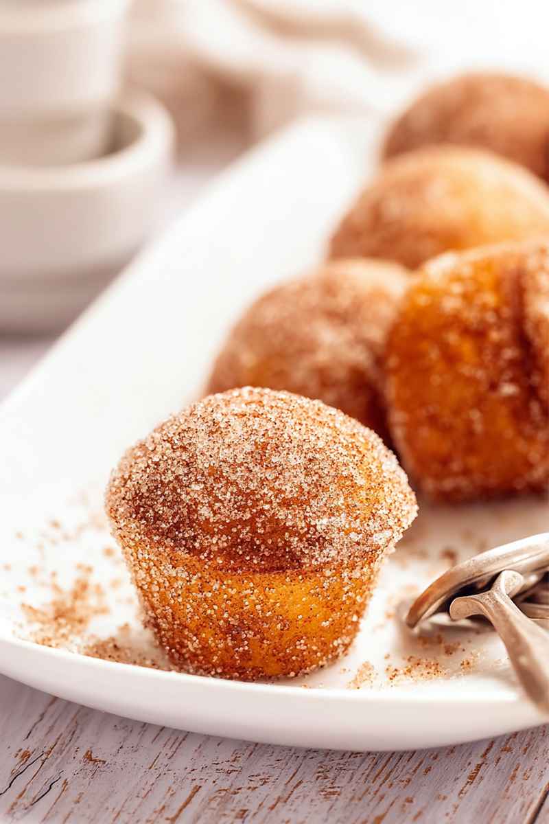 Mini muffins coated in cinnamon sugar, arranged on a white plate with a rustic wooden backdrop.