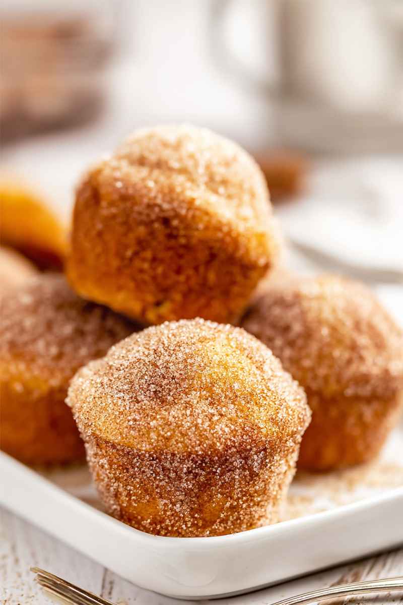 Mini muffins coated in cinnamon sugar, arranged on a white plate.