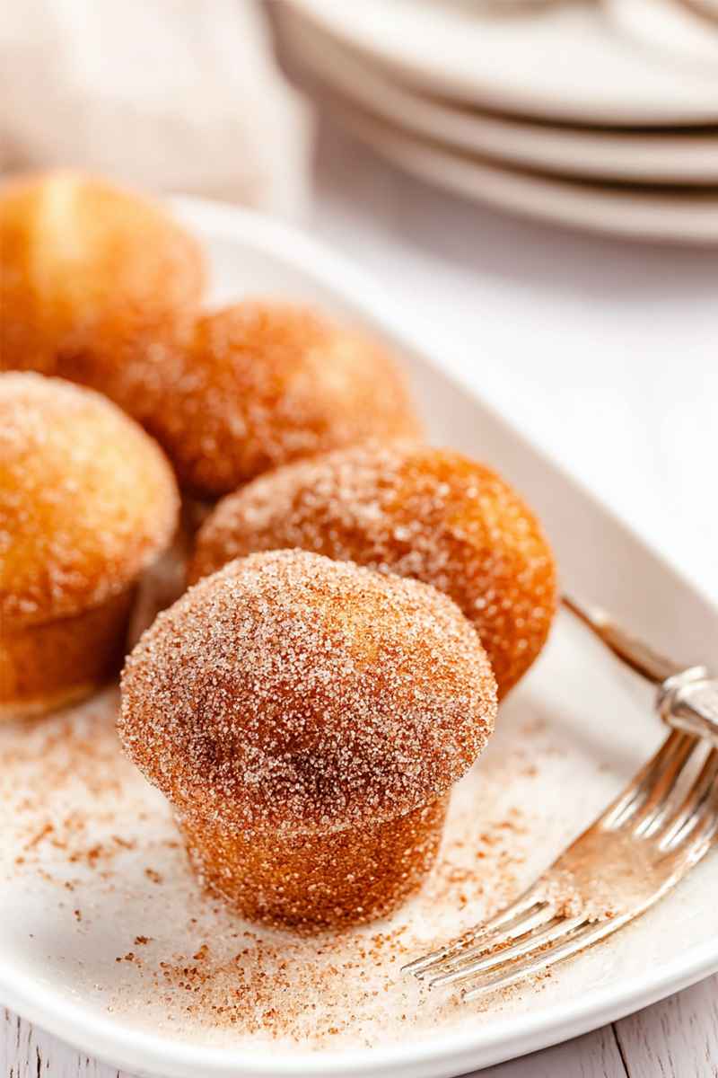 Cluster of mini muffins coated in cinnamon sugar, served on a white plate.