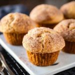 Golden-brown Cinnamon Sugar Swirl Muffins on a white plate, topped with a generous dusting of cinnamon sugar.