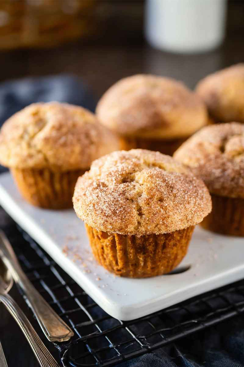 Golden-brown Cinnamon Sugar Swirl Muffins on a white plate, topped with a generous dusting of cinnamon sugar.