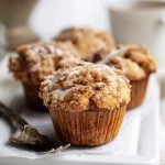 Golden-brown Coffee Cake Muffins topped with cinnamon sugar crumble and vanilla glaze, served on a white plate.