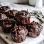 A stack of rich, dark Chocolate Muffins on a white plate, highlighting their dense, fudgy texture.