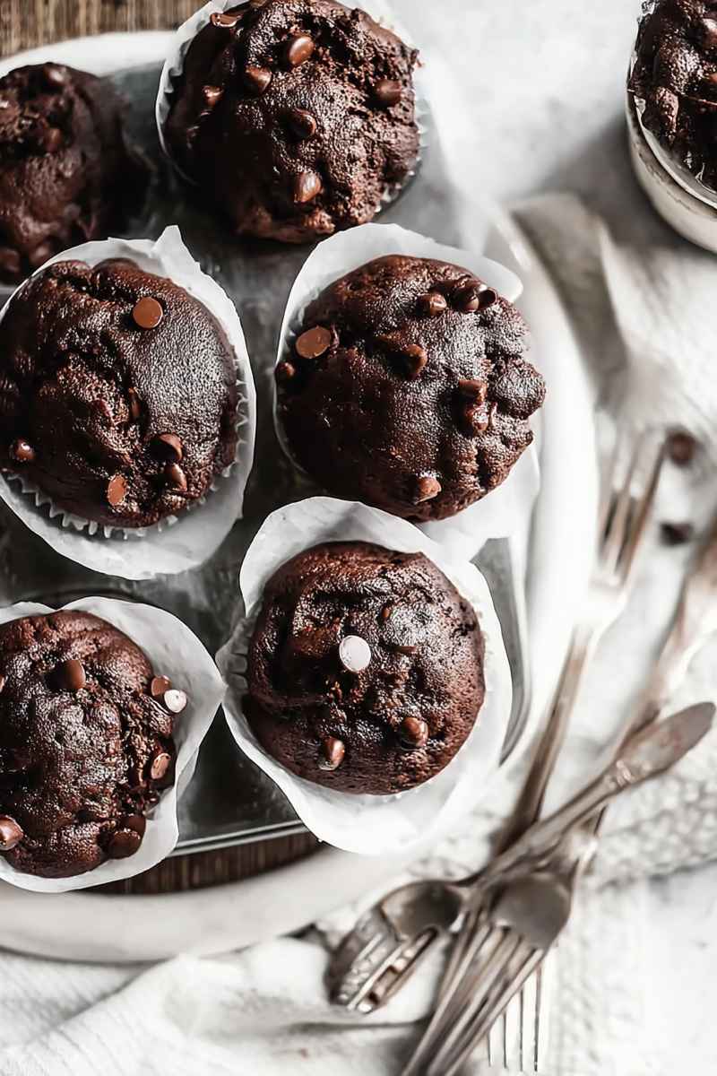 Cluster of dark chocolate muffins with scattered chocolate chips, served in white paper liners.