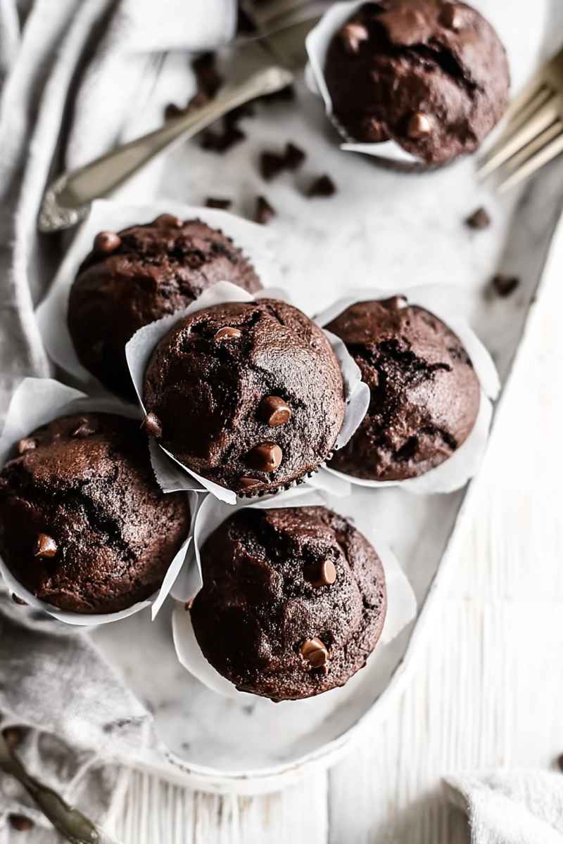 Close-up of dark chocolate muffins with embedded chocolate chips, served in white paper liners.