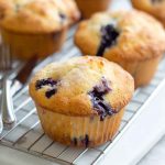 Golden-blueberry muffins with visible blueberries and sugar topping, cooling on a rack.