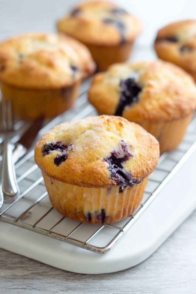 Golden-blueberry muffins with visible blueberries and sugar topping, cooling on a rack.