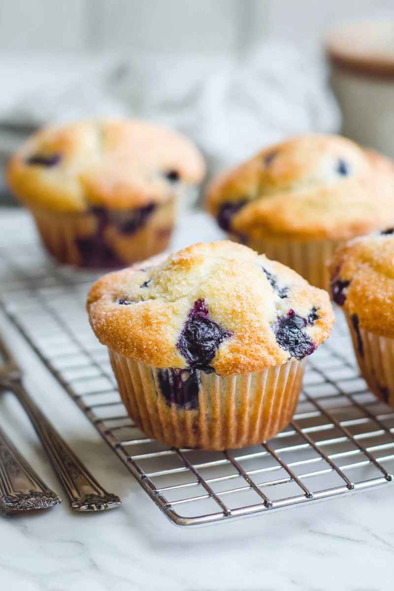 Golden-blueberry muffin with visible blueberries and sugar topping, cooling on a rack.