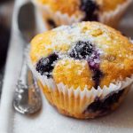 Golden-yellow lemon blueberry muffins topped with powdered sugar and fresh blueberries.