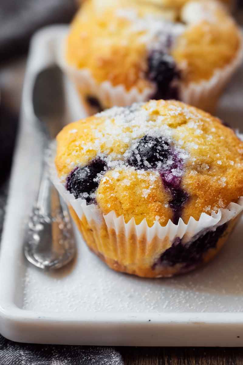 Golden-yellow lemon blueberry muffins topped with powdered sugar and fresh blueberries.