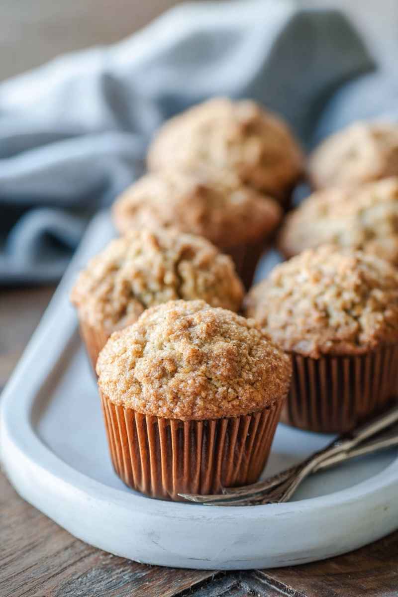 Golden oatmeal muffins with a crumbly sugar topping, served on a white plate with a rustic wooden backdrop.