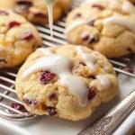 Orange Cranberry Meltaway Cookies being drizzled with a white glaze, showcasing their golden-brown texture and bright red cranberries.
