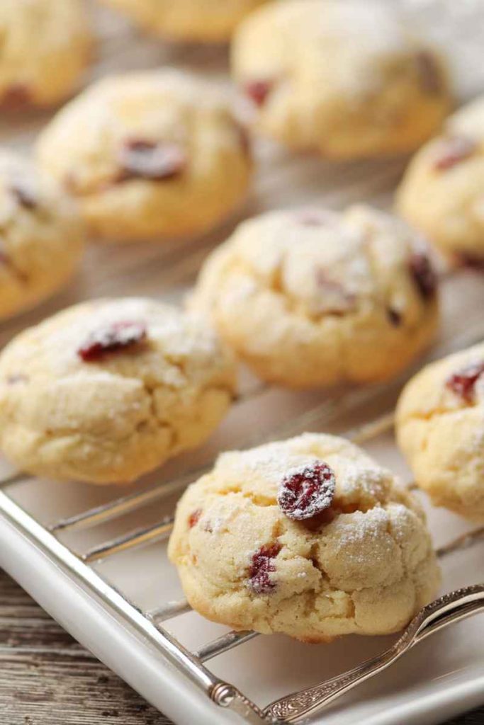 A batch of Orange Cranberry Meltaway Cookies with golden-brown texture, cranberries, and some dusted with powdered sugar.