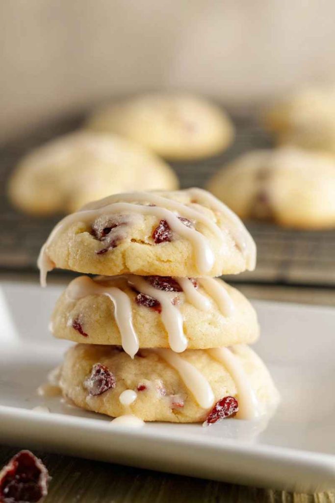 A stack of Orange Cranberry Meltaway Cookies with golden-brown texture, cranberries, and a glossy white glaze.