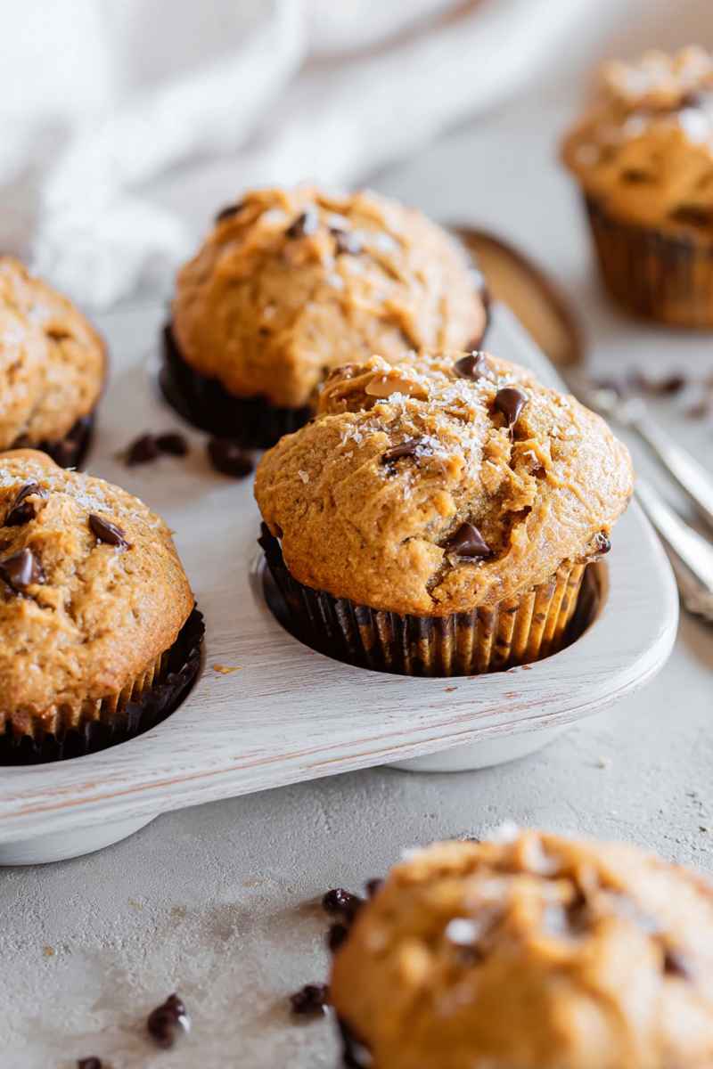 Tall, domed peanut butter muffins with chocolate chips, arranged on a white tray.