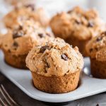 Golden-brown peanut butter muffins topped with chocolate chips and sugar, served on a white plate.