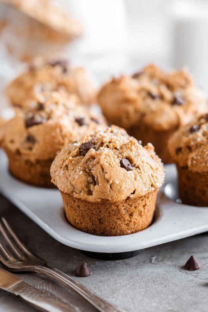 Golden-brown peanut butter muffins topped with chocolate chips and sugar, served on a white plate.
