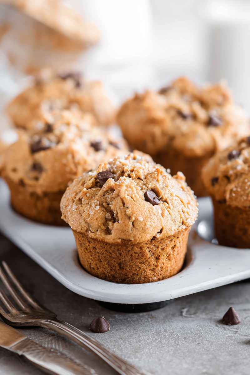 Golden-brown peanut butter muffins topped with chocolate chips and sugar, served on a white plate.