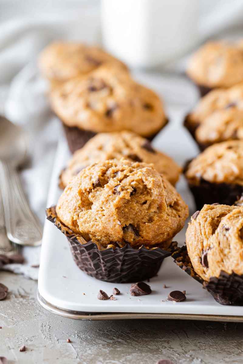 Close-up of a golden peanut butter muffin with melted chocolate chips, surrounded by more muffins.