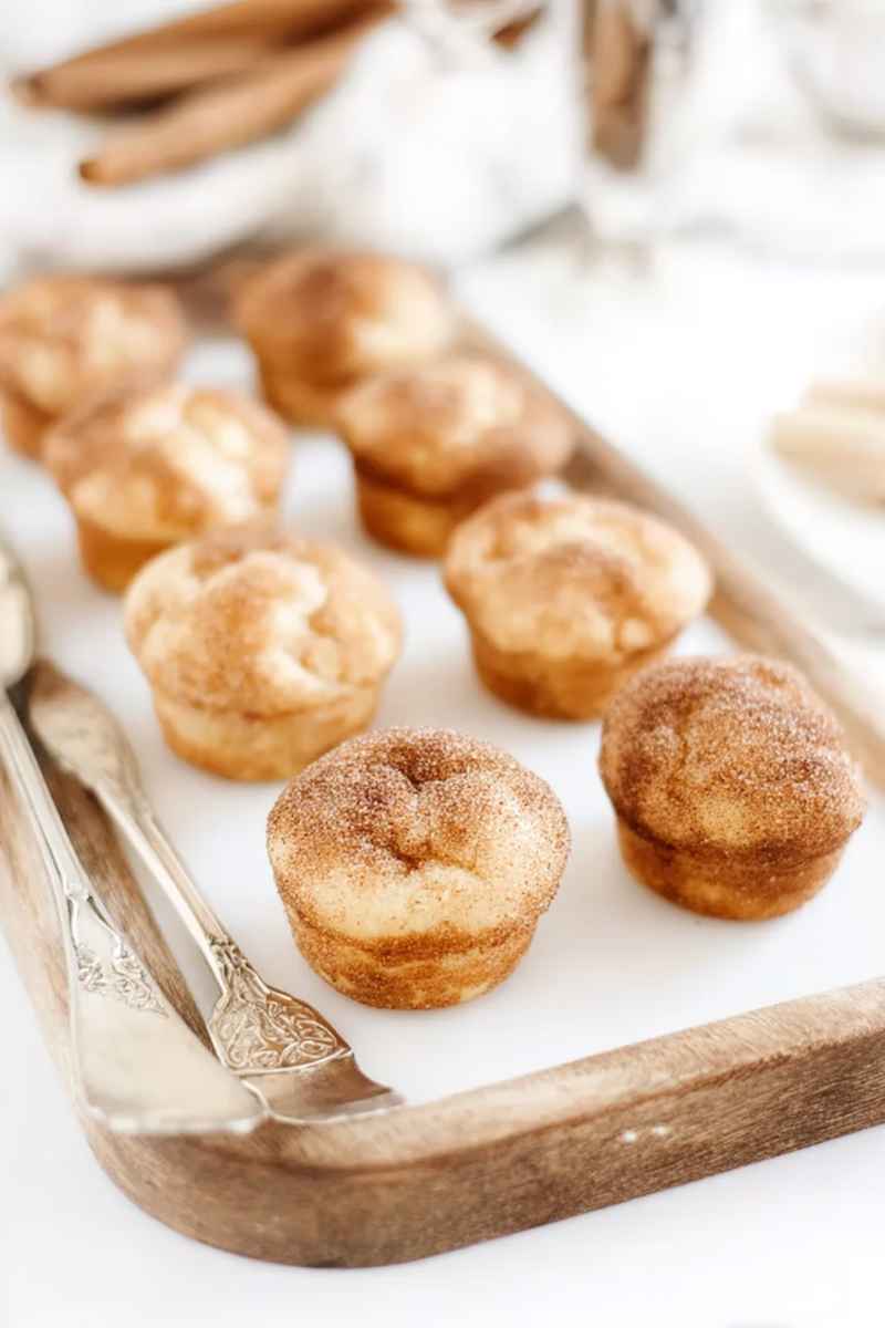 Soft snickerdoodle muffins with a generous cinnamon sugar coating, presented on a wooden tray with a decorative knife.
