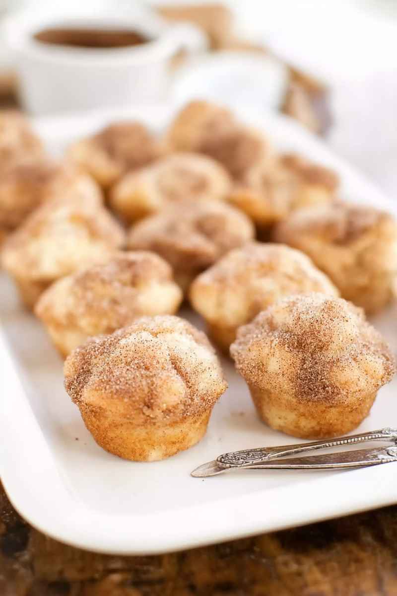 Golden snickerdoodle muffins with a rich cinnamon sugar topping, neatly arranged on a white plate.