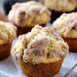 Golden muffins topped with a crunchy cinnamon streusel, served on a white plate with a vintage spoon.
