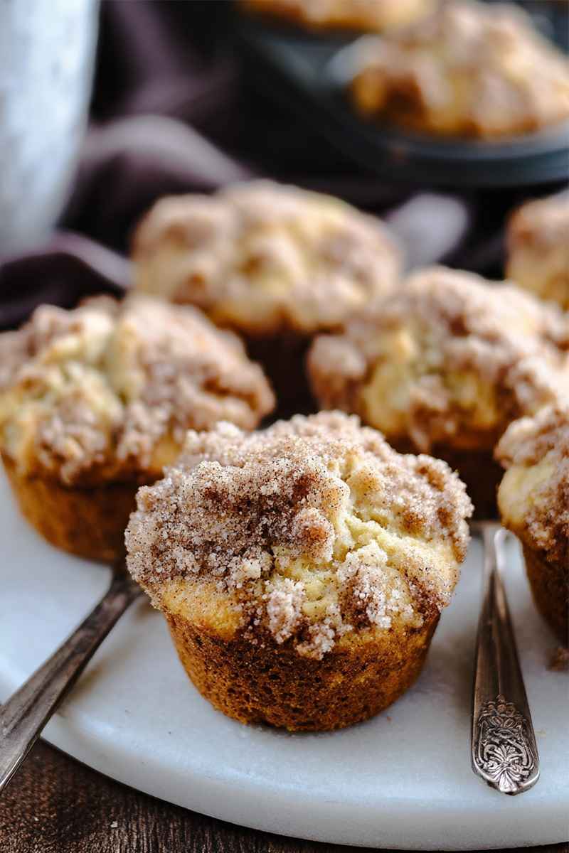 A batch of golden muffins topped with cinnamon streusel, presented on a white plate.
