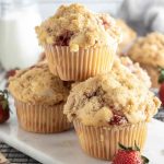 A stack of golden-brown Strawberry Streusel Muffins with a crumbly streusel topping, surrounded by fresh strawberries.