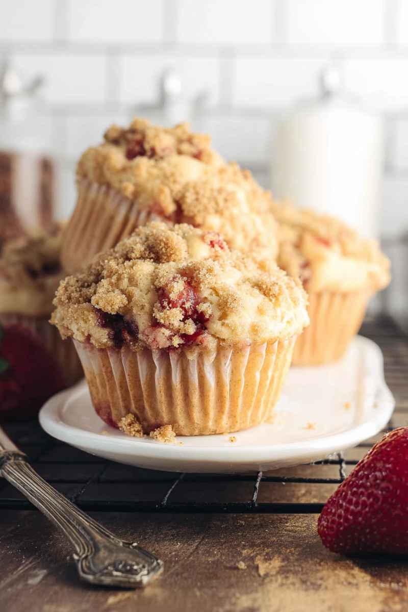 A stack of Strawberry Streusel Muffins with a crumbly streusel topping, accompanied by a fresh strawberry.