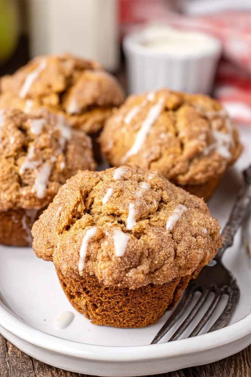 Golden-brown Apple Butter Muffins with a crumbly streusel topping and drizzled with a white glaze, served on a white plate.