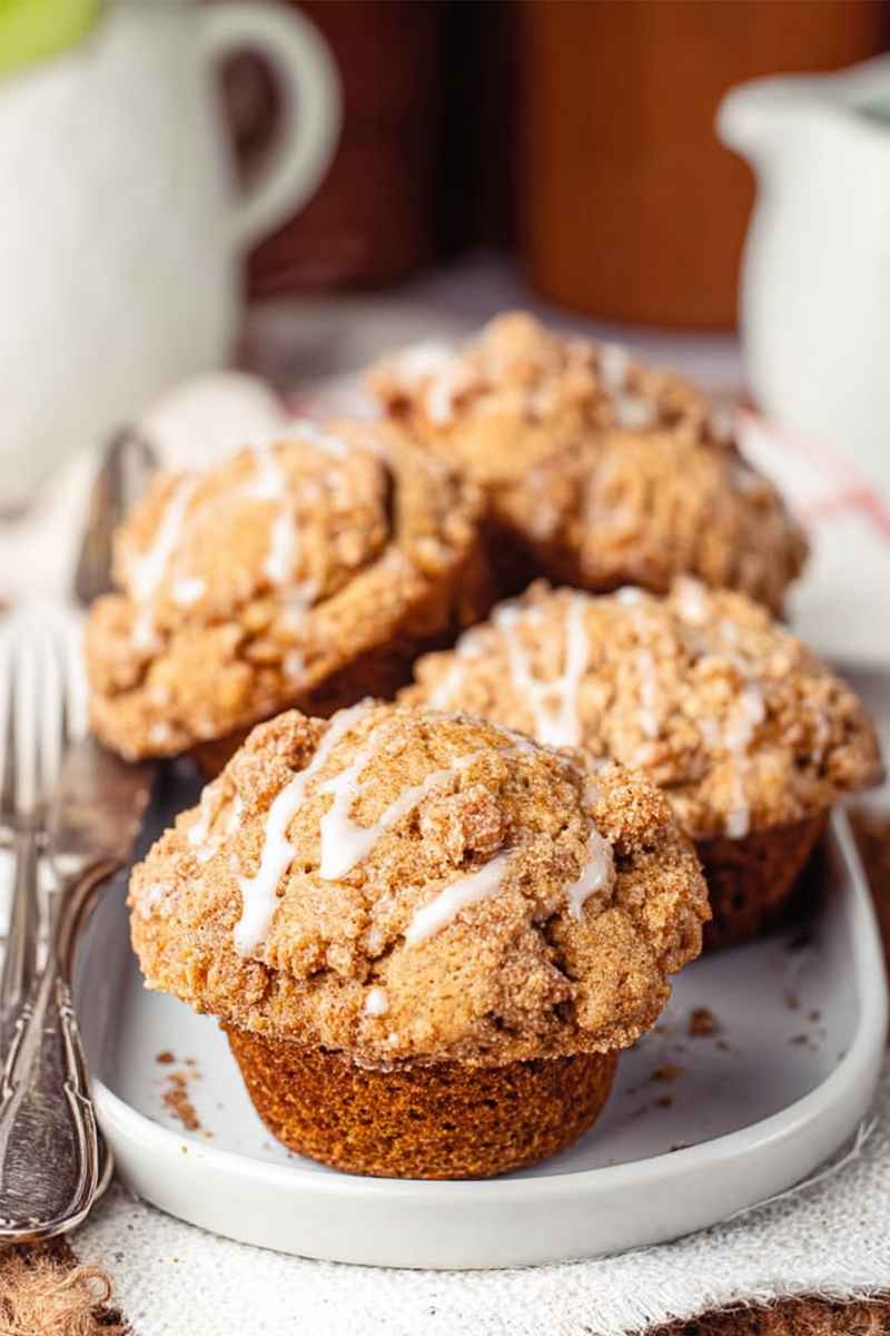 Golden Apple Butter Muffins with a crumbly streusel and a drizzle of white glaze, presented on a white plate.