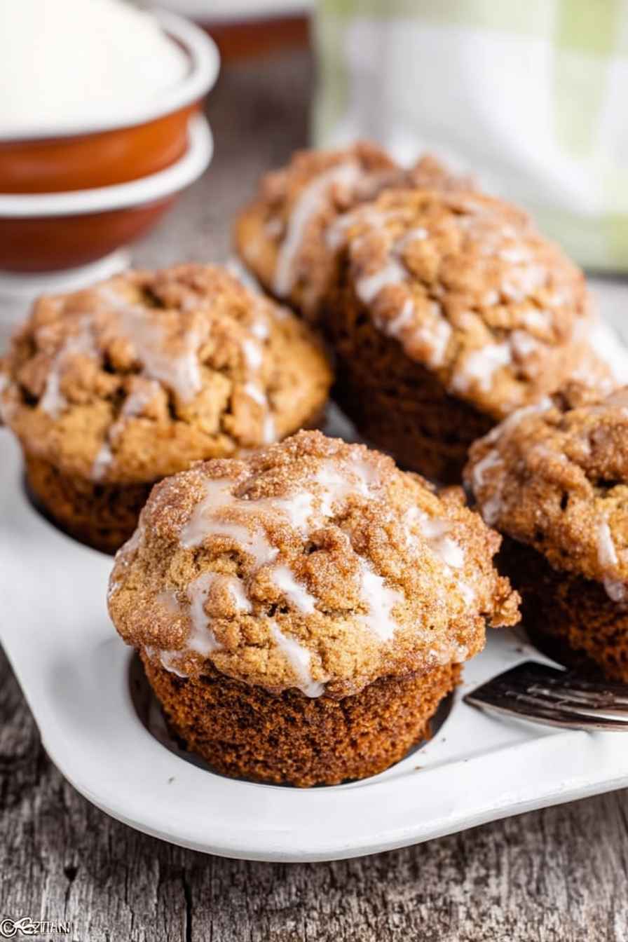 Fluffy Apple Butter Muffins with a golden streusel topping and a drizzle of white glaze, served on a white plate.